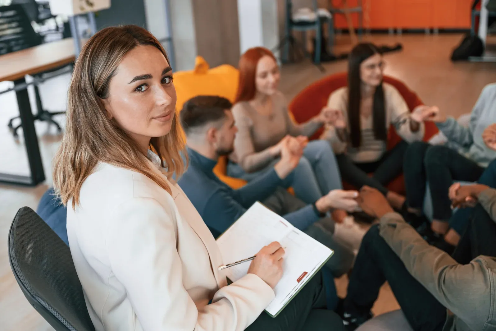 Una mujer observa y toma notas mientras un grupo de personas participa en una conversación sobre gestión emocional, fomentando una mente en crecimiento.